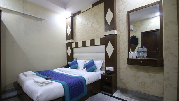 A neatly made bed with a blue and white bedspread, a wooden headboard, and a nightstand with a lamp. - Lord Krishna Hotel Dx. Inn (New Delhi)