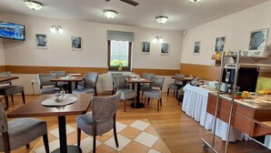 Un restaurante con varias mesas y sillas, una zona de bufé y un televisor instalado en la pared.