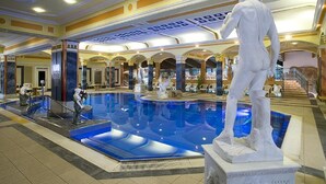 Una amplia piscina interior con una estatua de un hombre, rodeada de columnas y un techo decorativo con molduras.