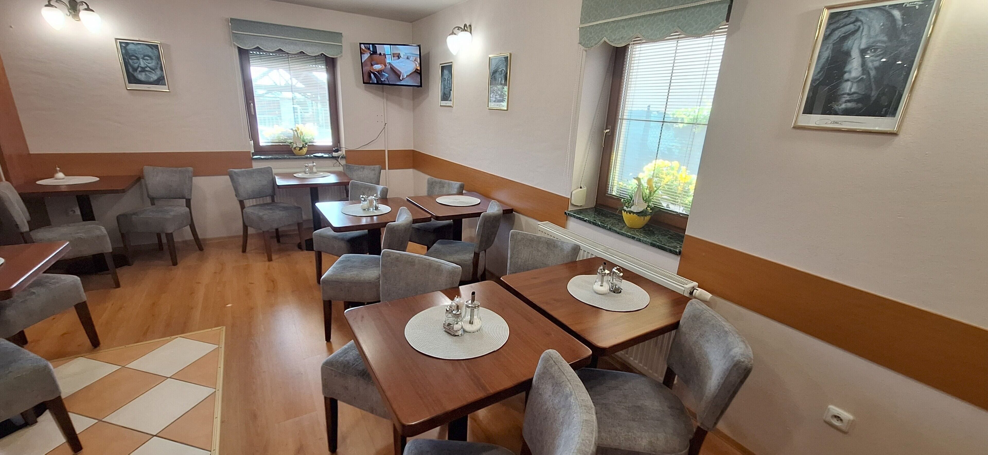 A dining area with multiple tables and chairs, a television mounted on the wall, and a window with a view.