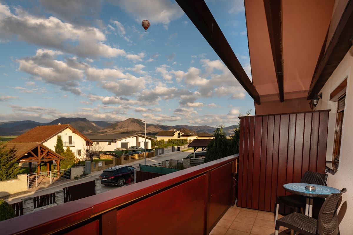 Un balcon donnant sur un quartier résidentiel, une montgolfière dans le ciel et une table avec des chaises.