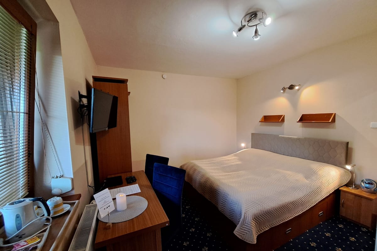 Une chambre d’hôtel comprenant un lit, un bureau avec une chaise, une petite table, un téléviseur fixé au mur et un luminaire au plafond.
