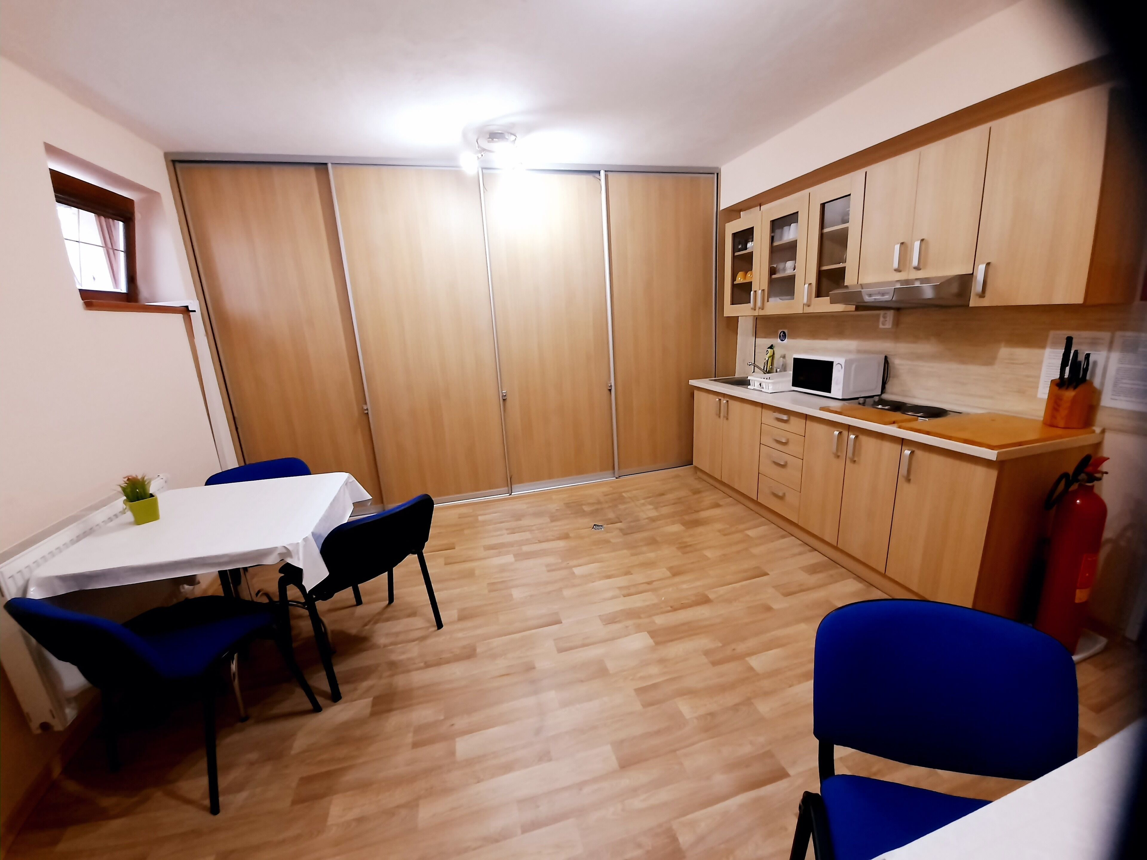 Une cuisine compacte avec des meubles en bois, un four à micro-ondes et un petit coin repas agrémenté de chaises bleues et d’une table blanche.