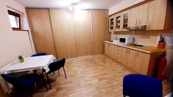 Une cuisine compacte avec des meubles en bois, un four à micro-ondes et un petit coin repas agrémenté de chaises bleues et d’une table blanche.