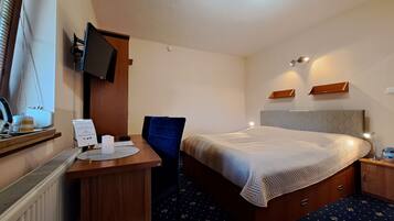 Habitación de hotel con cama, escritorio, silla, televisor y una mesita con una taza y un cartel.