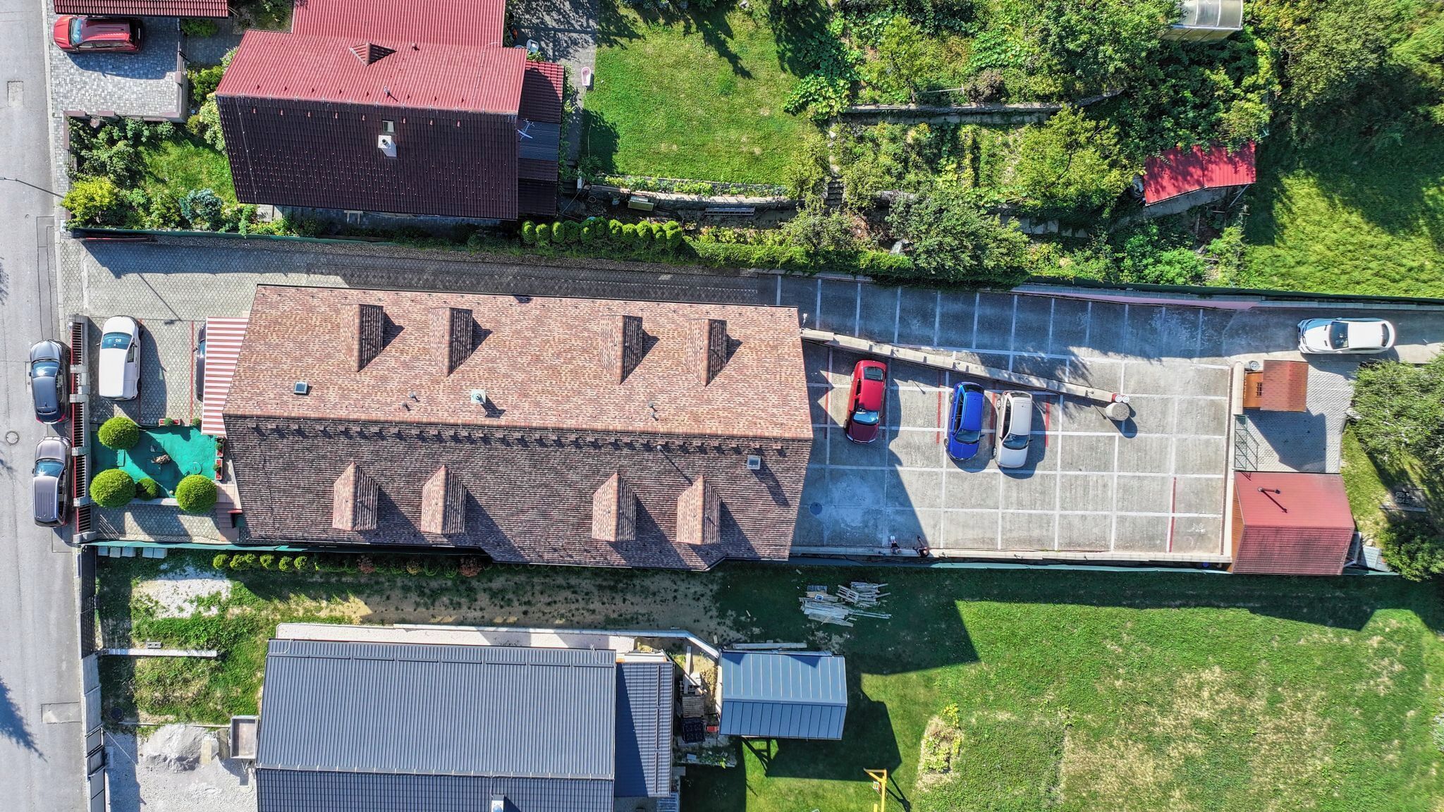 Vista aérea de un estacionamiento con varios autos, un edificio de techo rojo y una zona verde con césped.