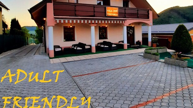A two-story building with a sign reading "Villa Viktoria." It features a balcony with outdoor seating and a paved entrance area.