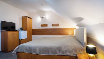 A bedroom with a bed, wooden headboard, bedside table with a lamp, a television, and a wardrobe.