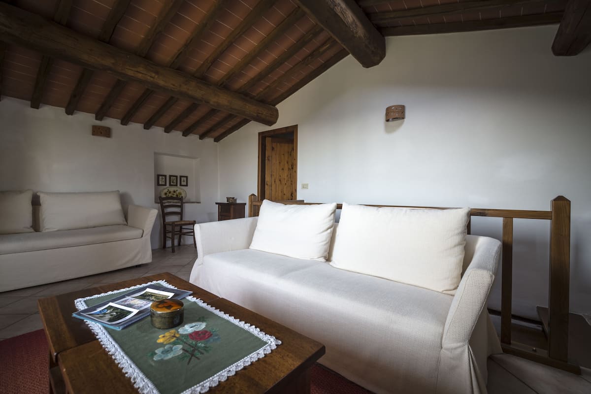A cozy living room with a wooden ceiling, a white sofa, and a coffee table with magazines.