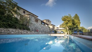 Una piscina amb parets de pedra, gandules i un edifici d'arquitectura de pedra.