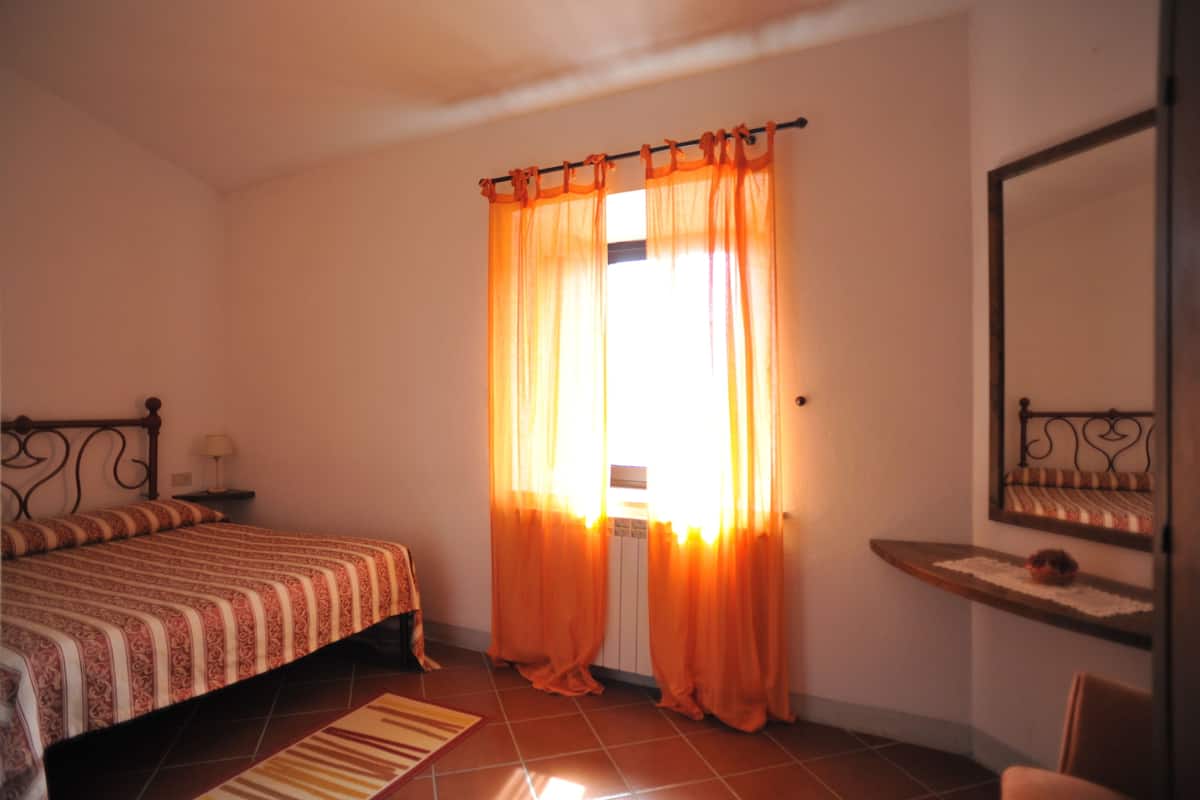 A bedroom with a bed, a nightstand, a radiator, and a window with orange curtains.