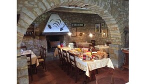 Una zona de dinar amb parets de pedra, taules preparades per a un àpat, una llar de pedra i un rètol que diu 'Colleluono'.