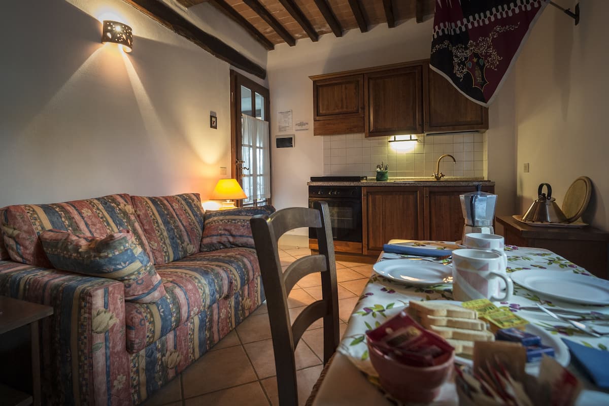 A cozy living room with a sofa, a dining table set with plates and cups, and a kitchen in the background.