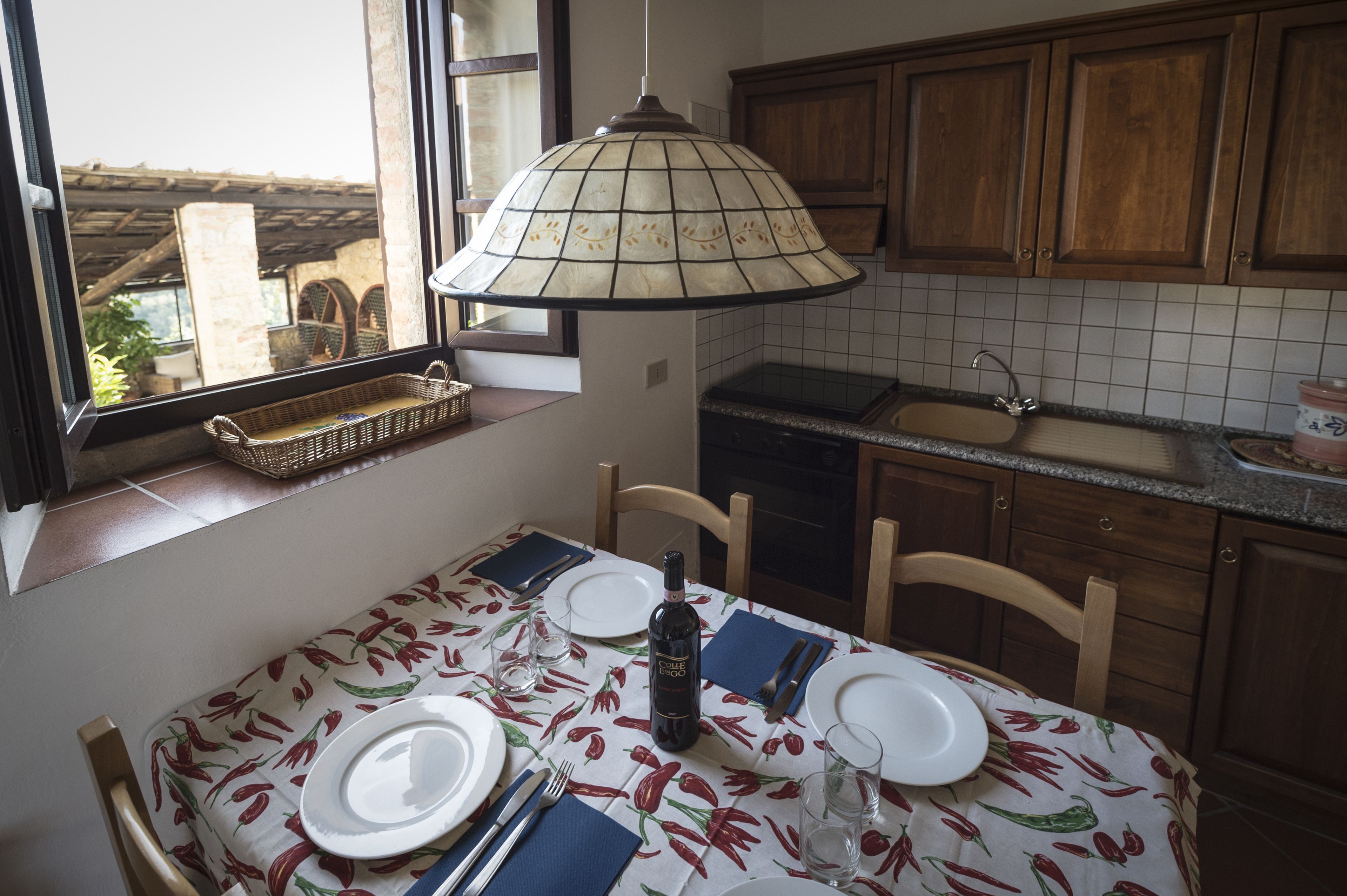A dining area with a table set for two, a window with a view, wooden cabinets, and a tiled backsplash.