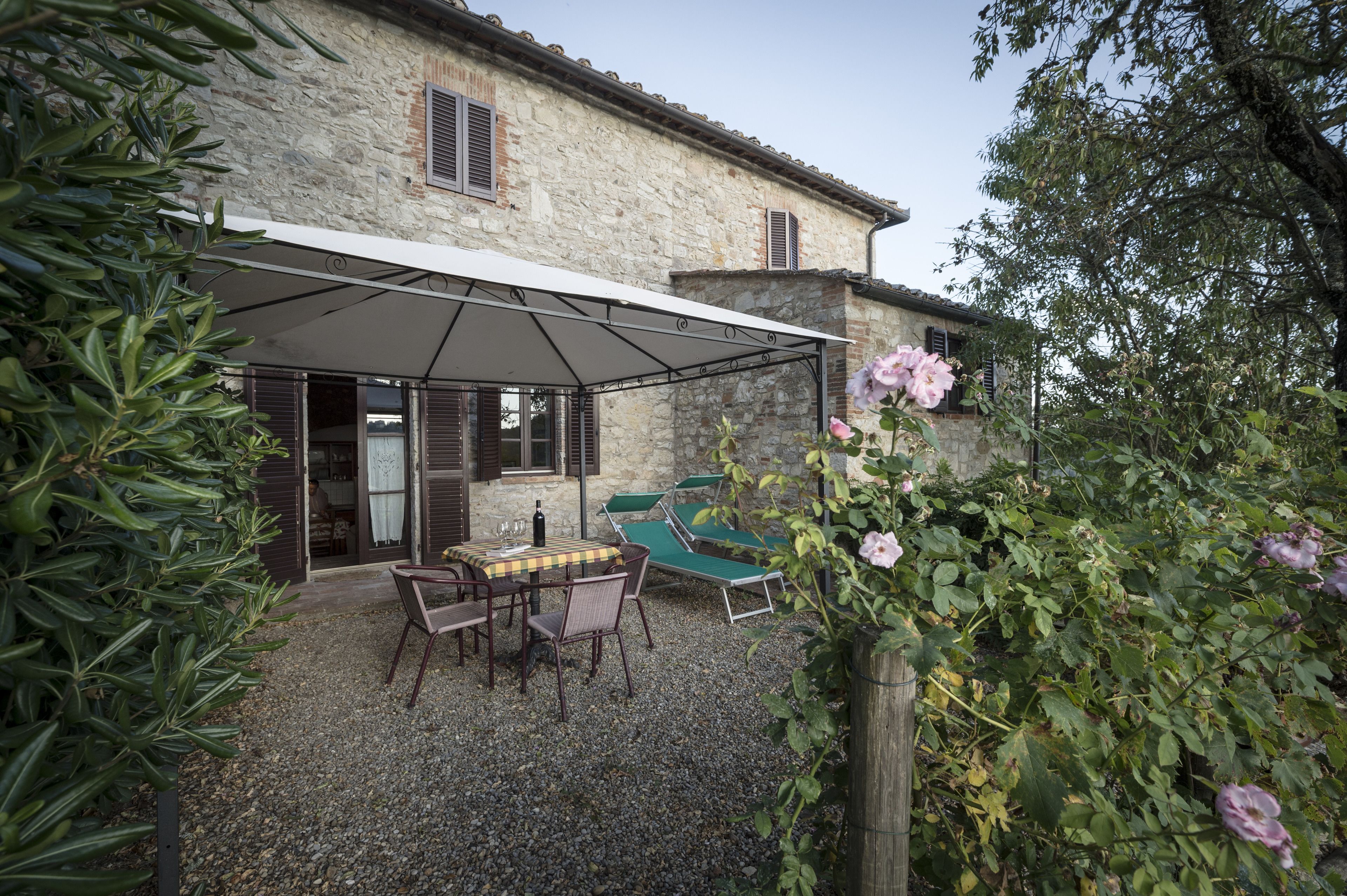 A stone building with a covered patio, outdoor seating, and a gravel ground.