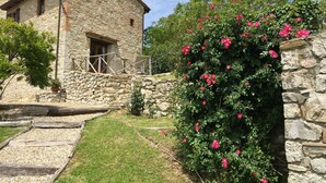 Edifici de pedra amb un balcó i un jardí ple de flors roses.