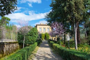 A pathway leading to a building with a symmetrical facade, surrounded by well-maintained hedges and flowering trees. - Dimora Salviati (Florence)