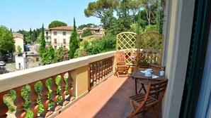 A balcony with a wooden table and chairs, a wicker chair, and a view of a town with buildings and trees. - Dimora Salviati (Florence)