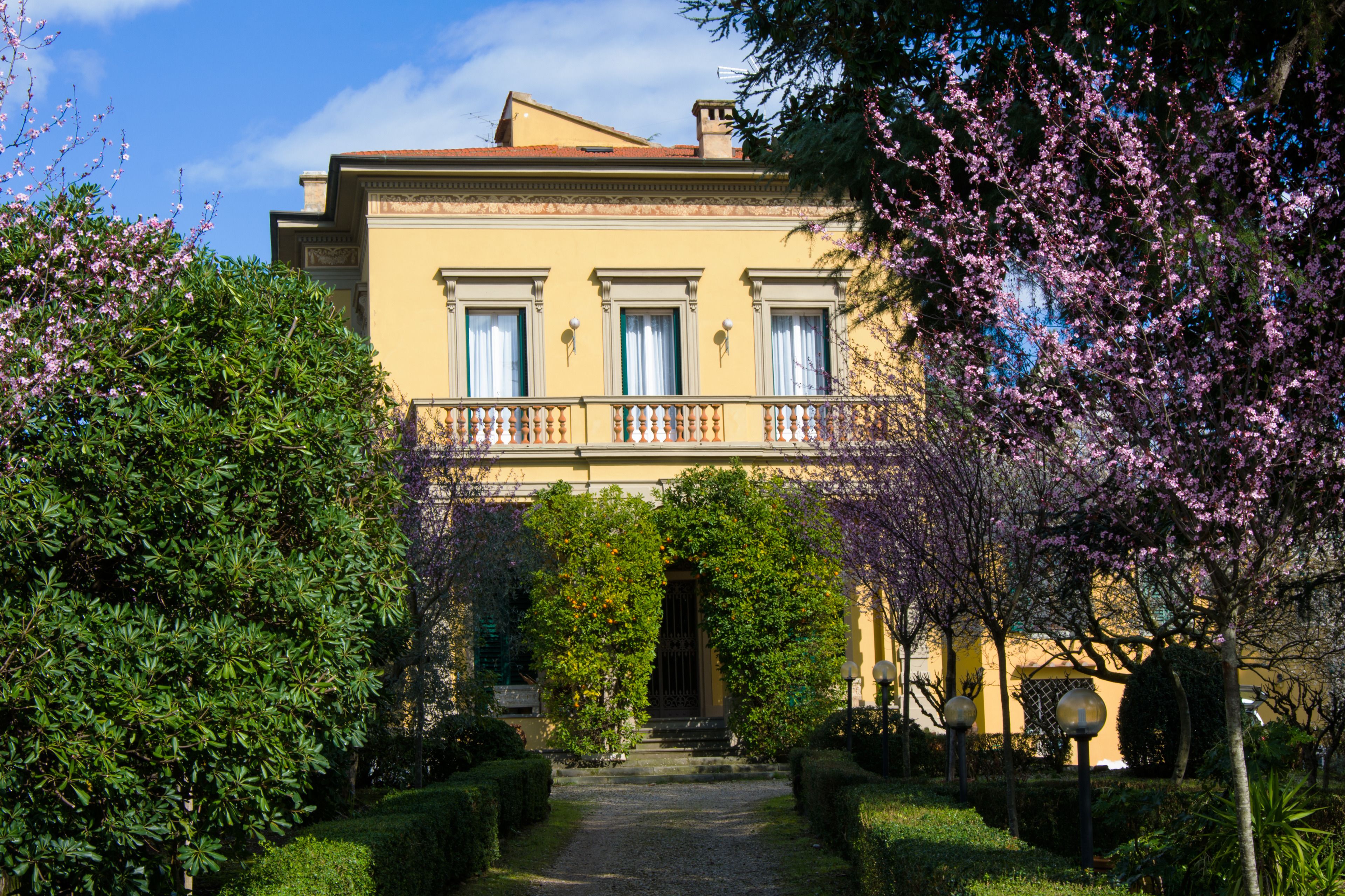 A classical building with a symmetrical facade, a central entrance, and a well-maintained garden with flowering trees.
