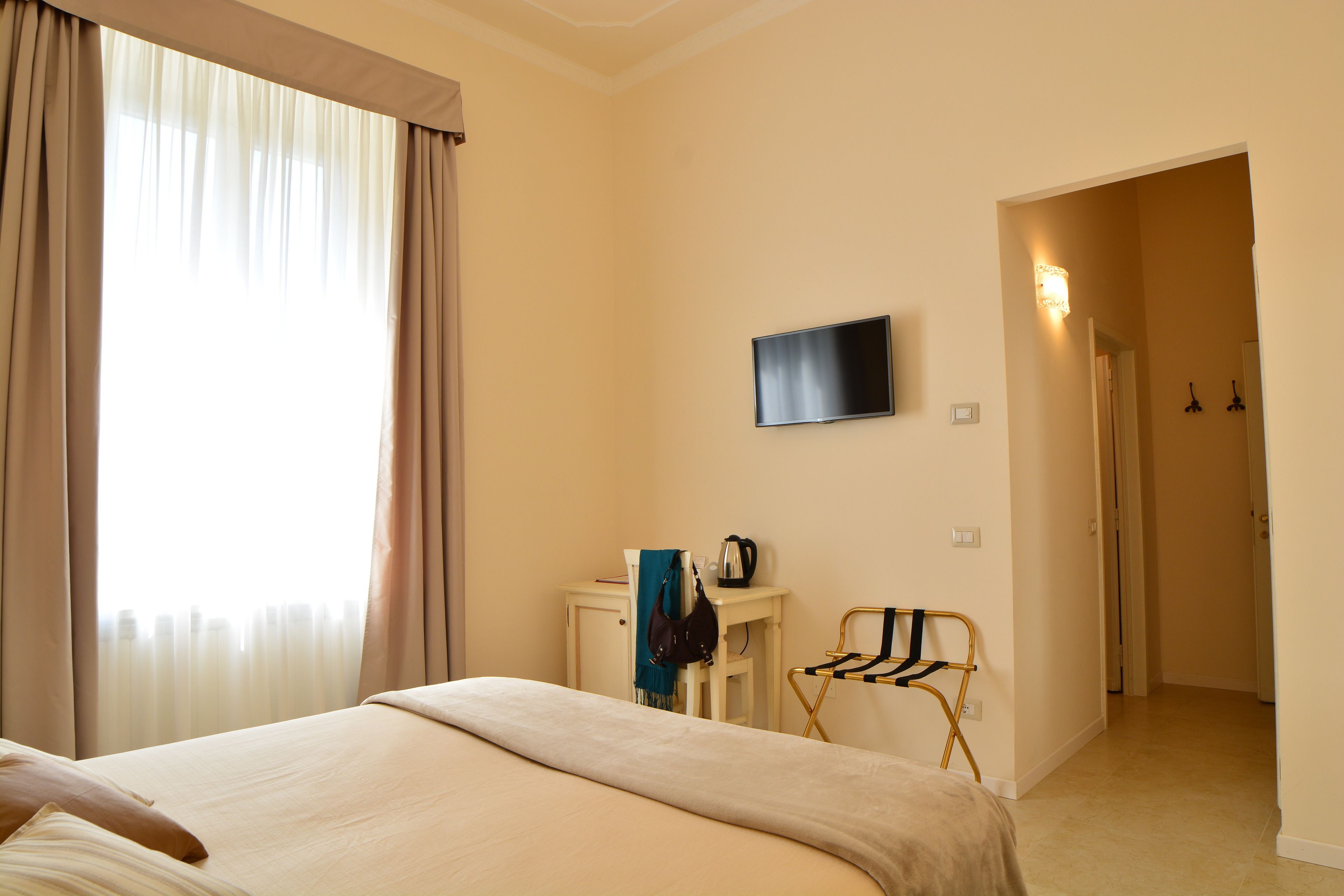 A hotel room with a bed, a desk with a television, a chair, and a view of the city through the window.