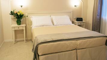 A neatly made bed with white linens, a bedside table with a lamp, and a vase of flowers.