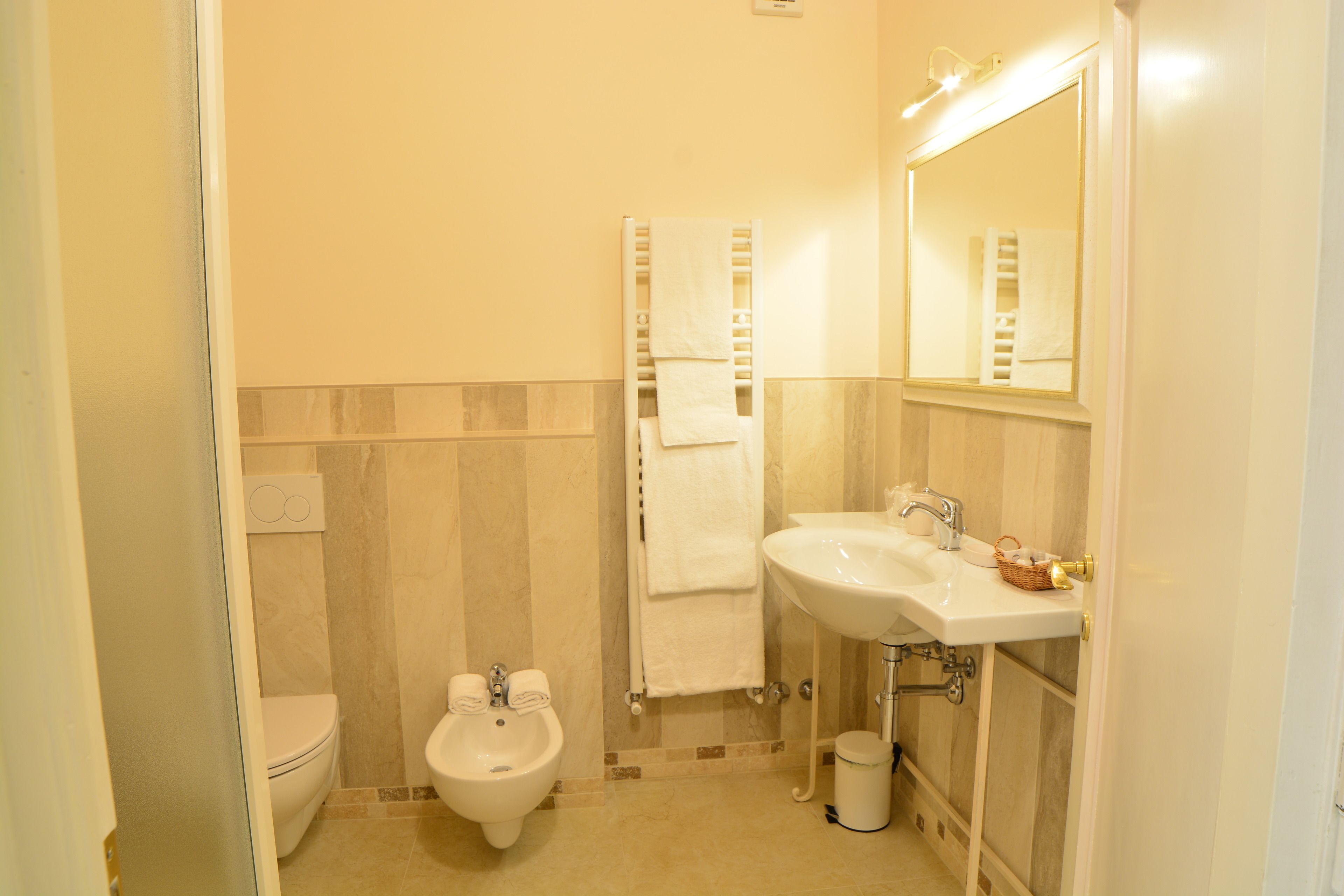 Un baño con inodoro, bidé, lavamanos y un perchero para toallas.