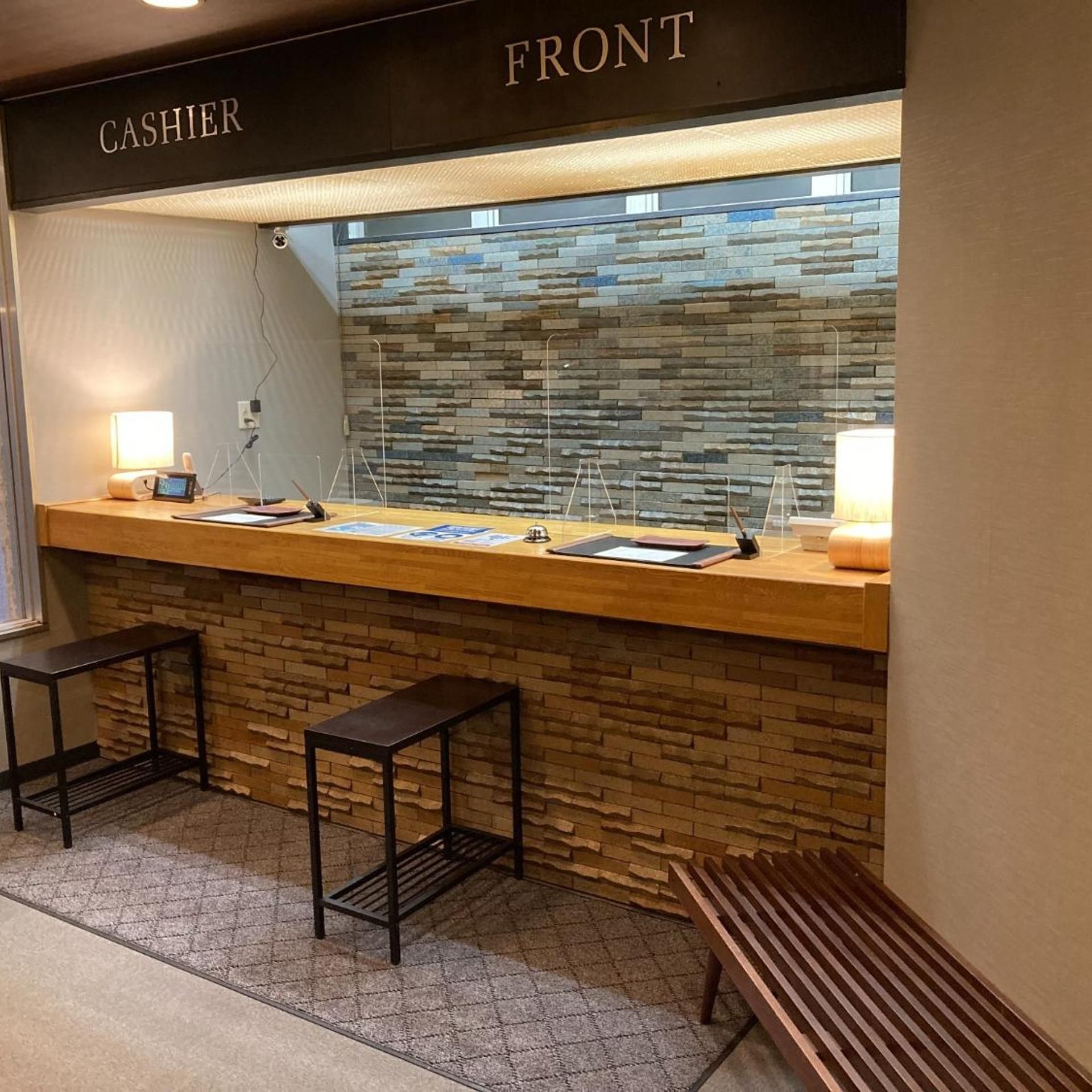 A cashier counter with a stone wall backdrop, a bench, and a sign indicating the front area.