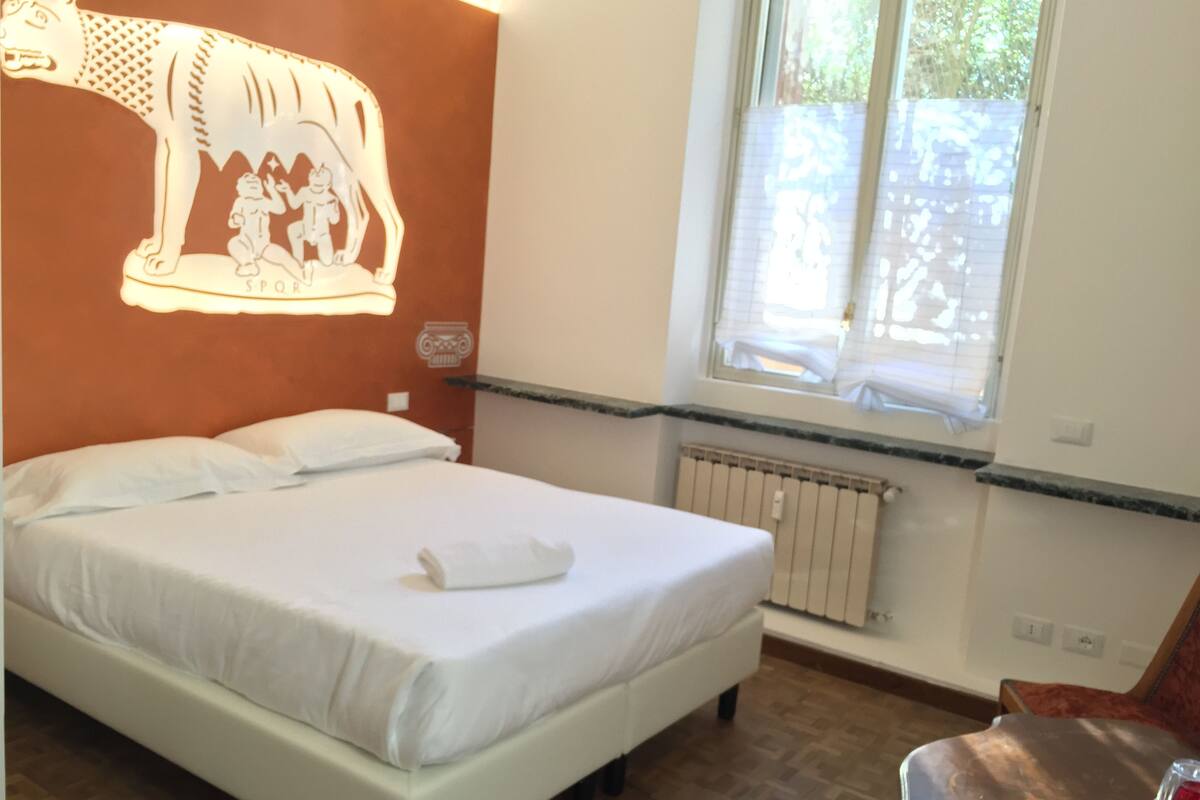 A bedroom with a bed, a window, a radiator, and a wall decoration.