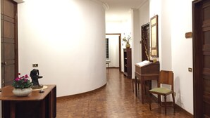 Un couloir doté d’un plancher en bois, un bureau orné d’un vase de fleurs, une chaise et une porte avec une plaque indiquant le numéro.