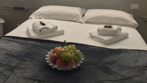 Une chambre d’hôtel avec un lit, des oreillers, un plateau avec des serviettes et un panier de fruits.