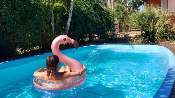 A swimming pool with a flamingo float, surrounded by lush greenery and a wooden deck. - Pousada Vistacalma (Imbituba)
