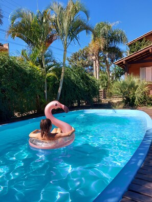 A swimming pool with a flamingo float, surrounded by lush greenery and a wooden deck. - Pousada Vistacalma (Imbituba)
