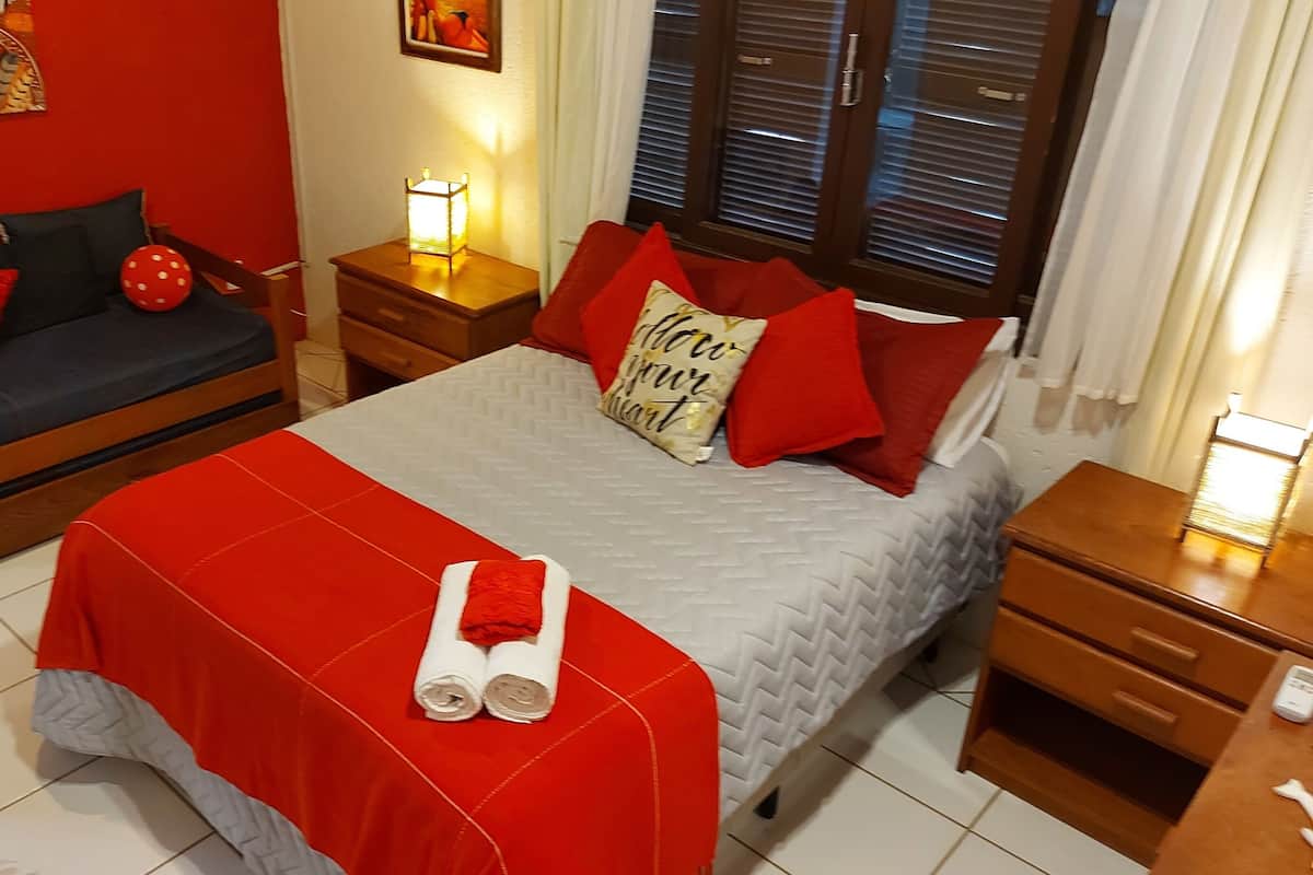 Habitación de hotel con cama, sofá, mesita de noche con lámpara y ventana con persianas.