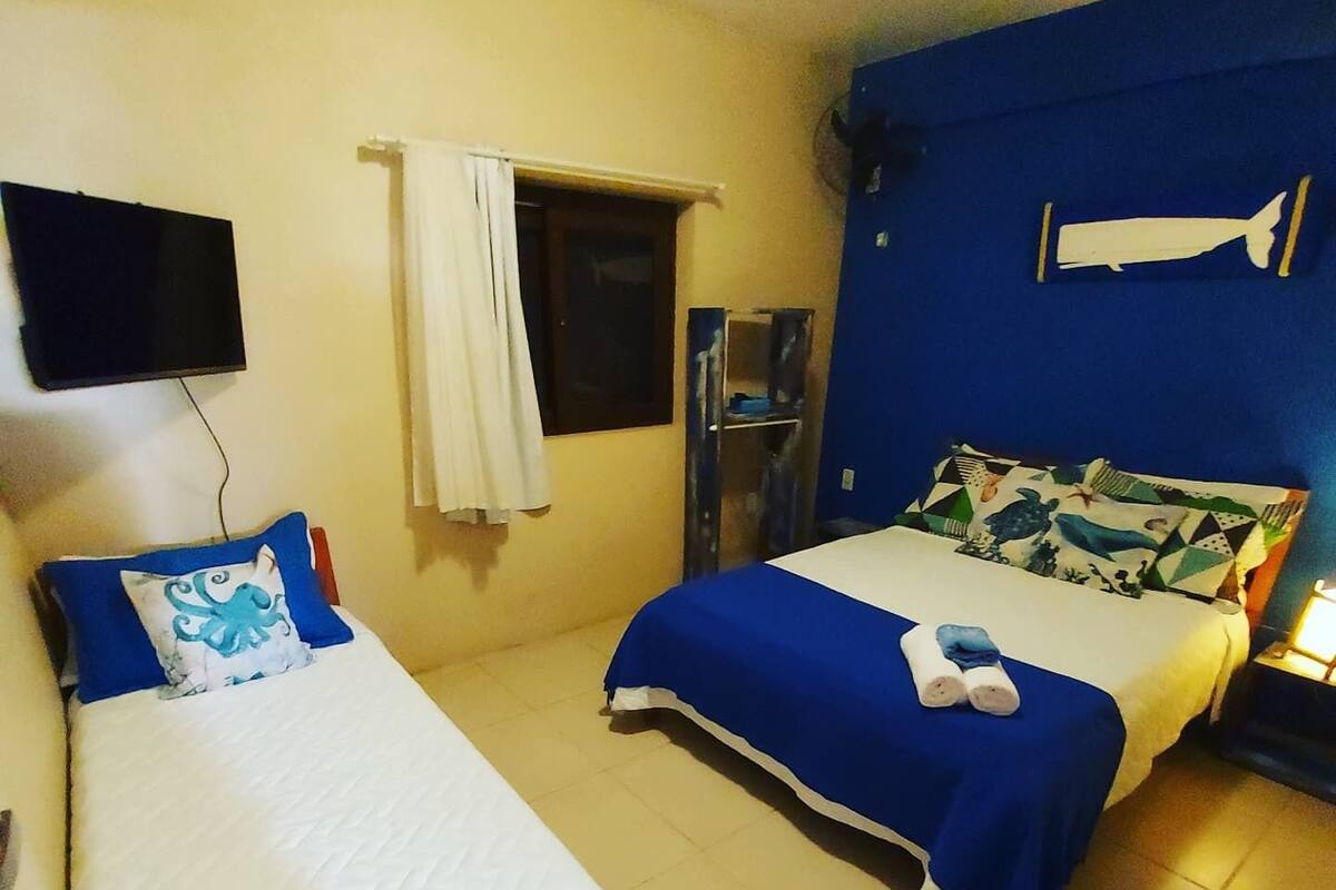 Habitación de hotel con dos camas, una con cubrecama azul y la otra con cubrecama blanca. Hay un televisor de pantalla plana montado en la pared sobre la cama con el cubrecama azul.