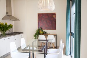 A modern kitchen with white cabinets, a glass dining table, and a hanging light fixture. - Guzman El Bueno Suites (Seville)