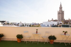 A rooftop terrace with potted plants, foldable chairs, and a view of a historic tower. - Guzman El Bueno Suites (Seville)