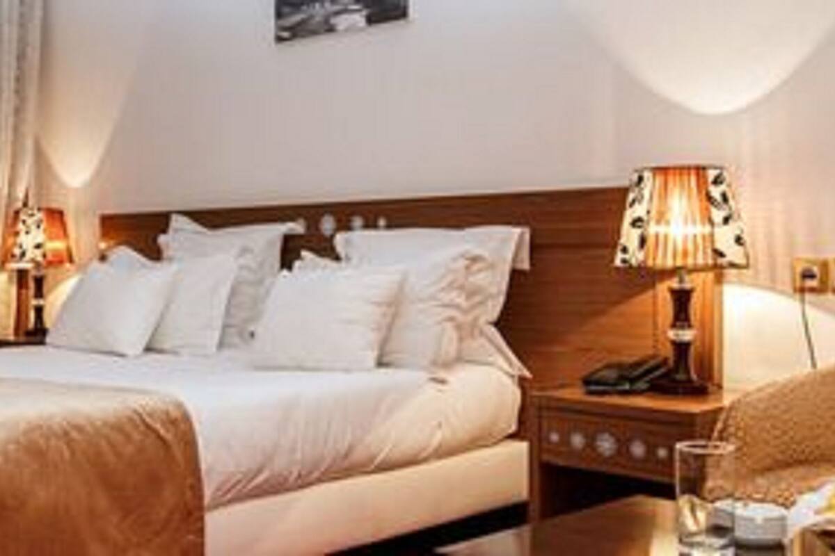 Une chambre d’hôtel avec un grand lit, deux lampes de chevet, une chaise et une petite table sur laquelle se trouve un panier de fruits.