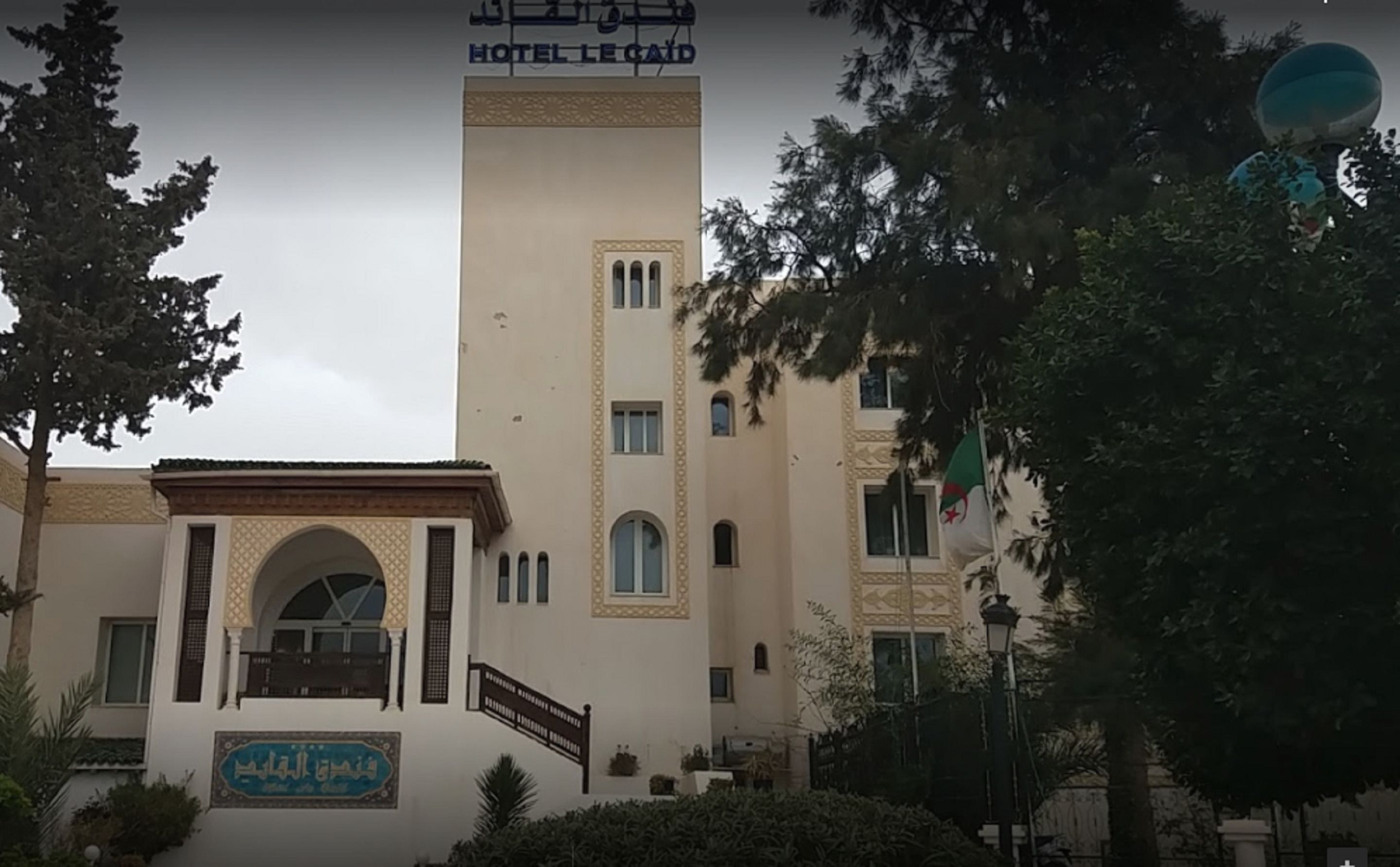 A hotel with a central tower, arched entrance, and a sign in Arabic.