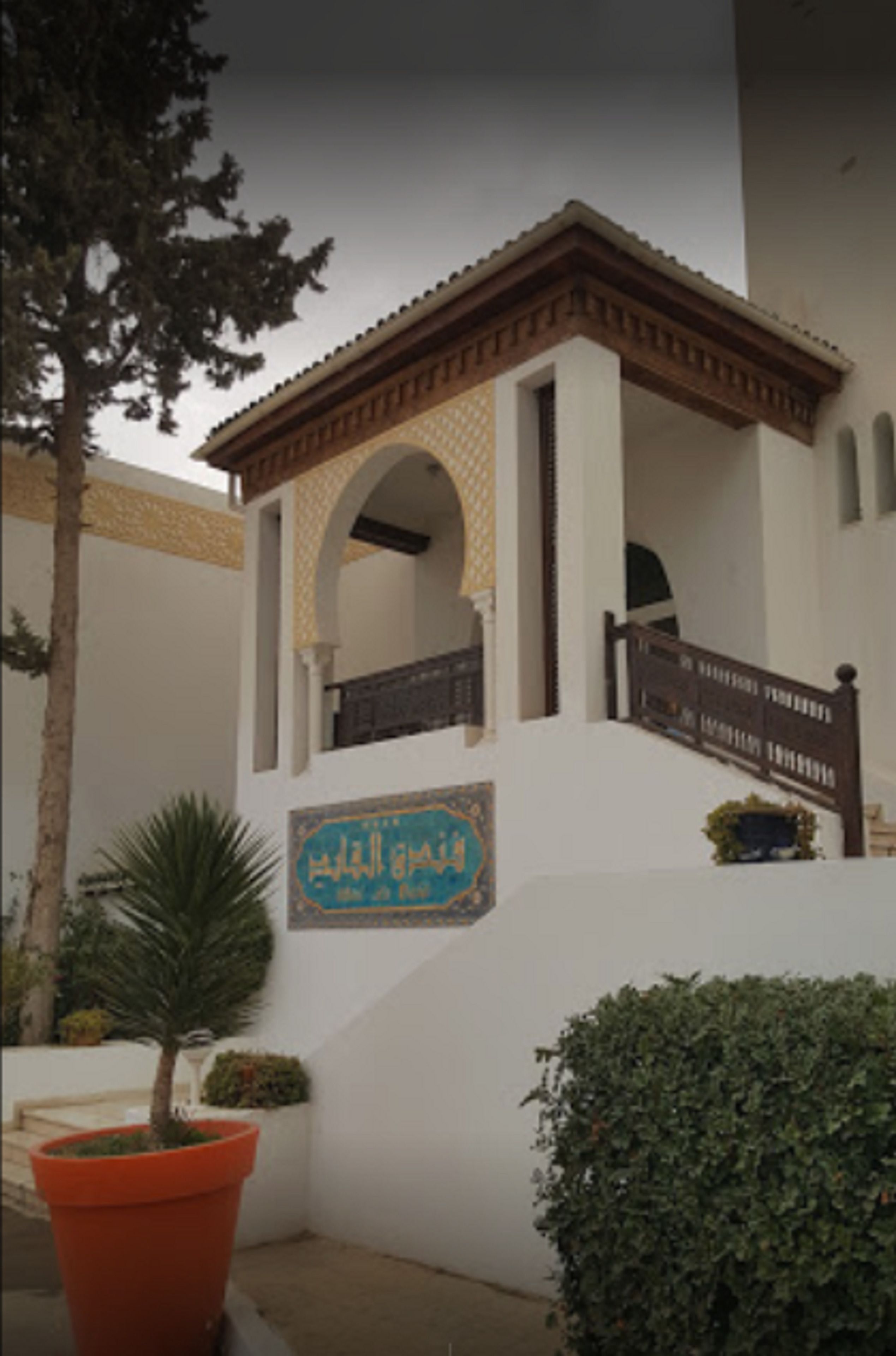 A building with a white facade, a wooden balcony, and a sign with Arabic text.