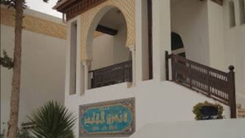 A building with a white facade, a wooden balcony, and a sign with Arabic text.
