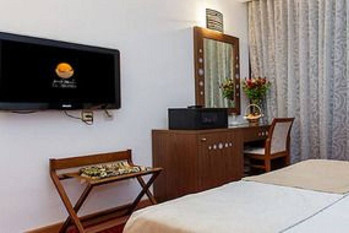 Une chambre d’hôtel avec un lit, un bureau, une chaise, une télévision et une fenêtre avec des rideaux.