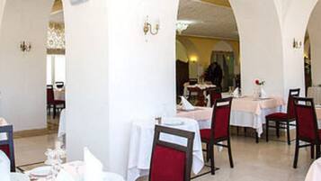 Ein Restaurant mit weißen Tischen und roten Stühlen, Bögen und Tapete mit Muster.
