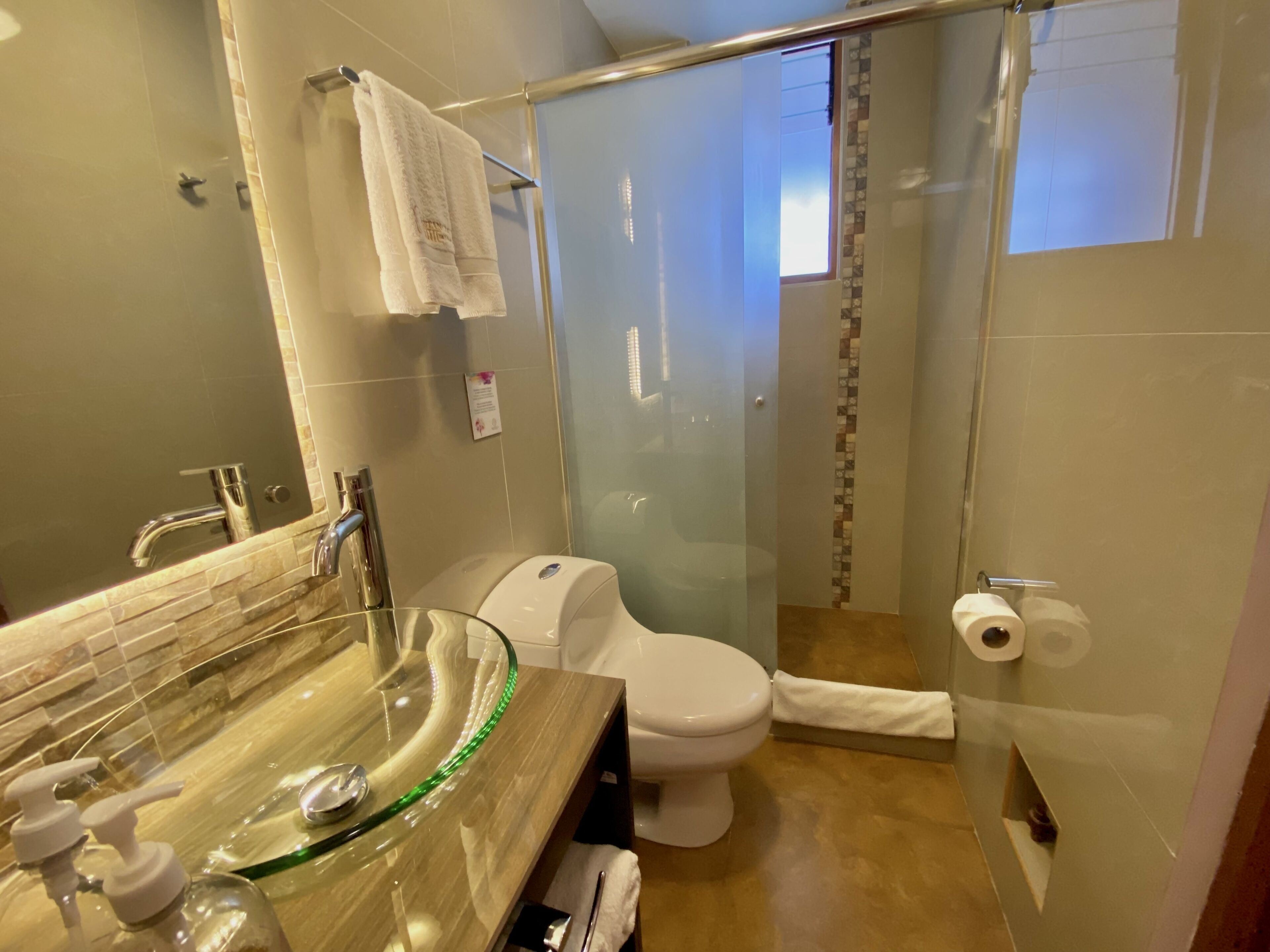 Un baño moderno con un lavabo de cristal, inodoro y ducha con cerramiento de vidrio.