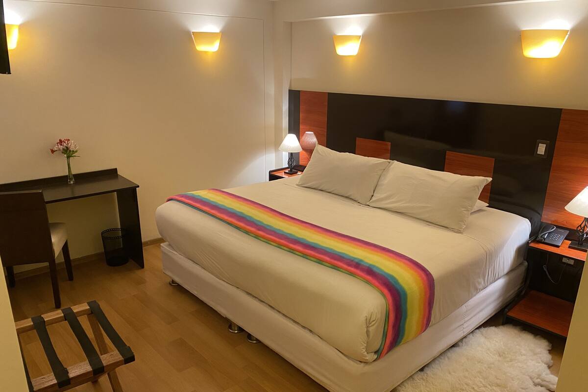 Habitación de hotel con una cama grande, un escritorio, una silla, una lámpara y un teléfono en la mesita de noche.