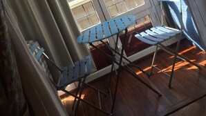 A room with a wooden floor, a blue ironing board, and a window with a view of a building with a red roof. - Pensión Ab Domini (San Sebastián)
