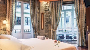 A hotel room with a stone wall, large windows with curtains, a bed with white linens, and a balcony with outdoor furniture. - Pensión Ab Domini (San Sebastián)