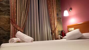 Habitación de hotel con cama, una toalla enrollada, una tetera roja y una mesita de noche.