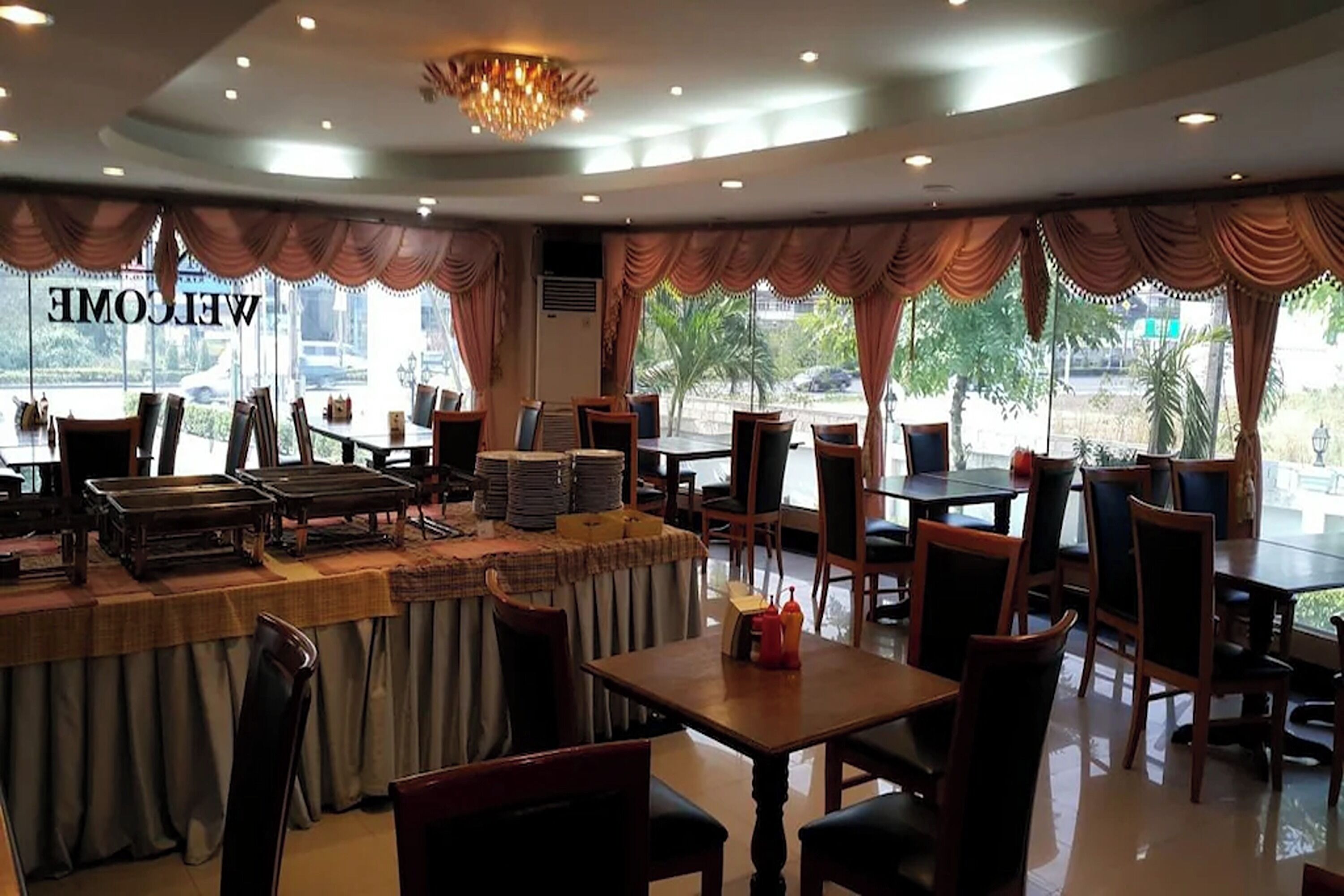 A restaurant with a 'WELCOME' sign, tables with chairs, and a view of the outdoors.