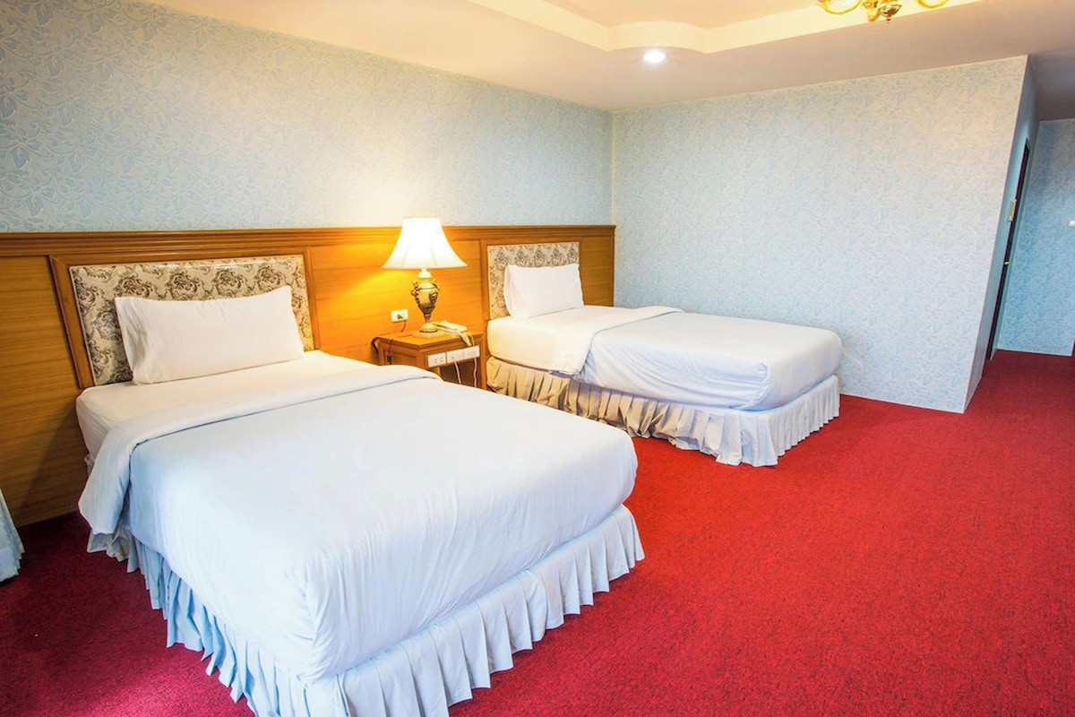 Habitación de hotel con dos camas, alfombra roja y cabecero de madera.