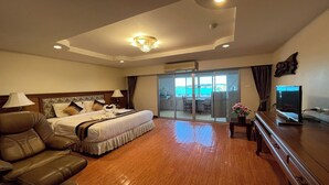 Habitación de hotel con cama, sofá, televisión, escritorio y vista al mar a través de un ventanal corredero.